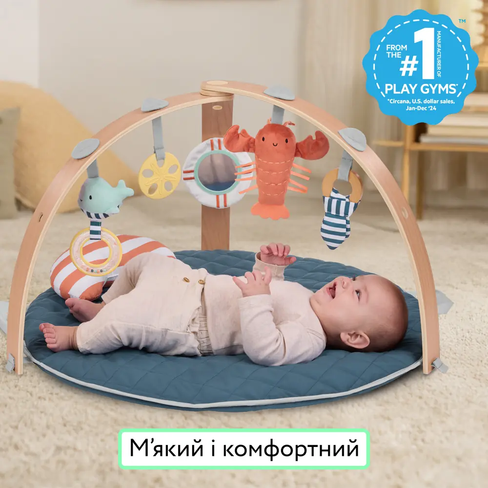 Малюк лежить на м'якому килимку Ingenuity Cozy Spot Harbor Haven під дерев'яними дугами з іграшками