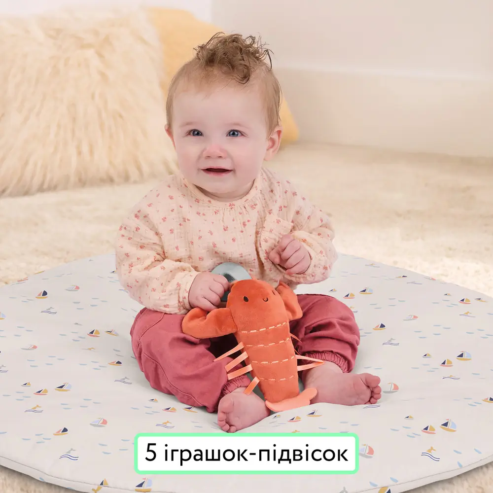 Дитина сидить на килимку Ingenuity Cozy Spot Harbor Haven з плюшевим омаром