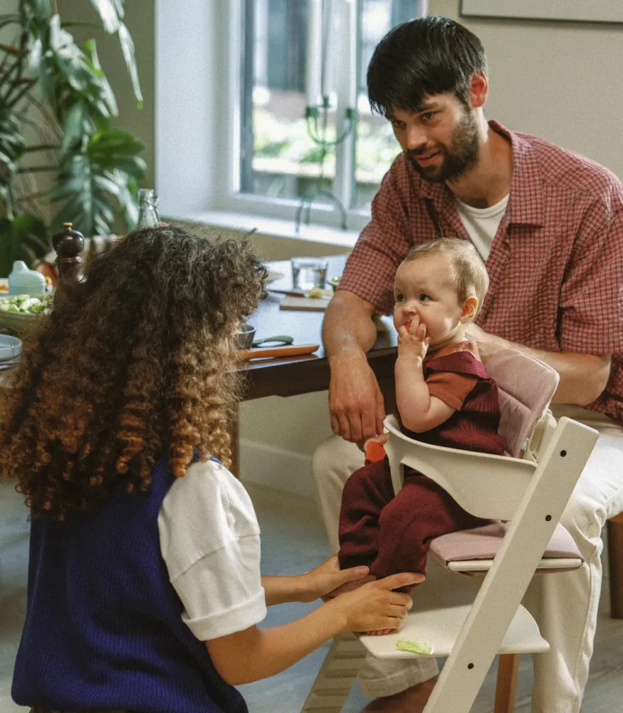 Малюк у стільчику Tripp Trapp зі спинкою Baby Set за столом поруч із дорослим і старшою дитиною